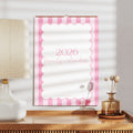2026 wall calendar with pink and white design on a wooden surface with a lamp and decorative items.