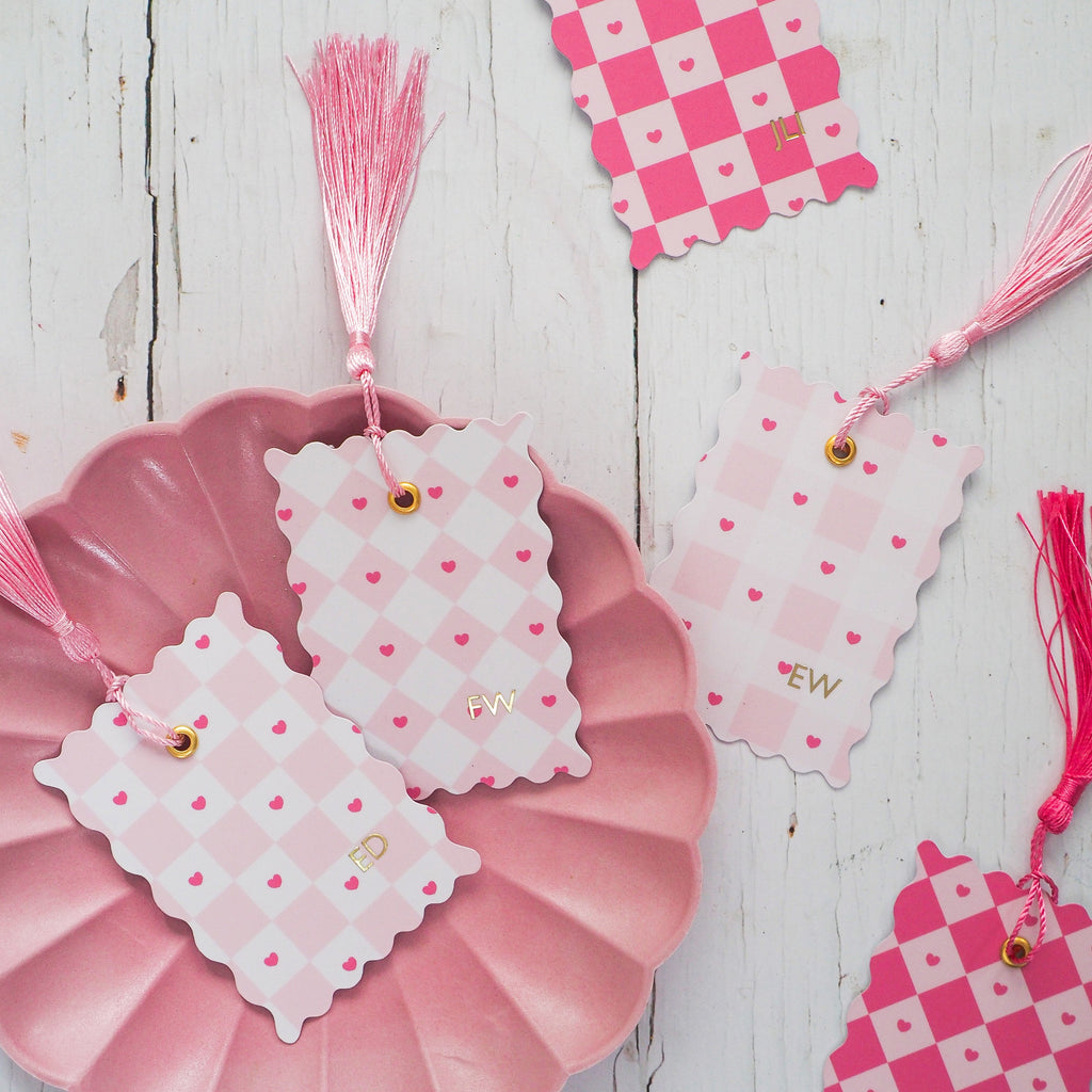 Decorative pink and white checkered tags with tassels on a wooden surface