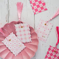 Decorative pink and white checkered tags with tassels on a wooden surface