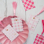 Decorative pink and white checkered tags with tassels on a wooden surface