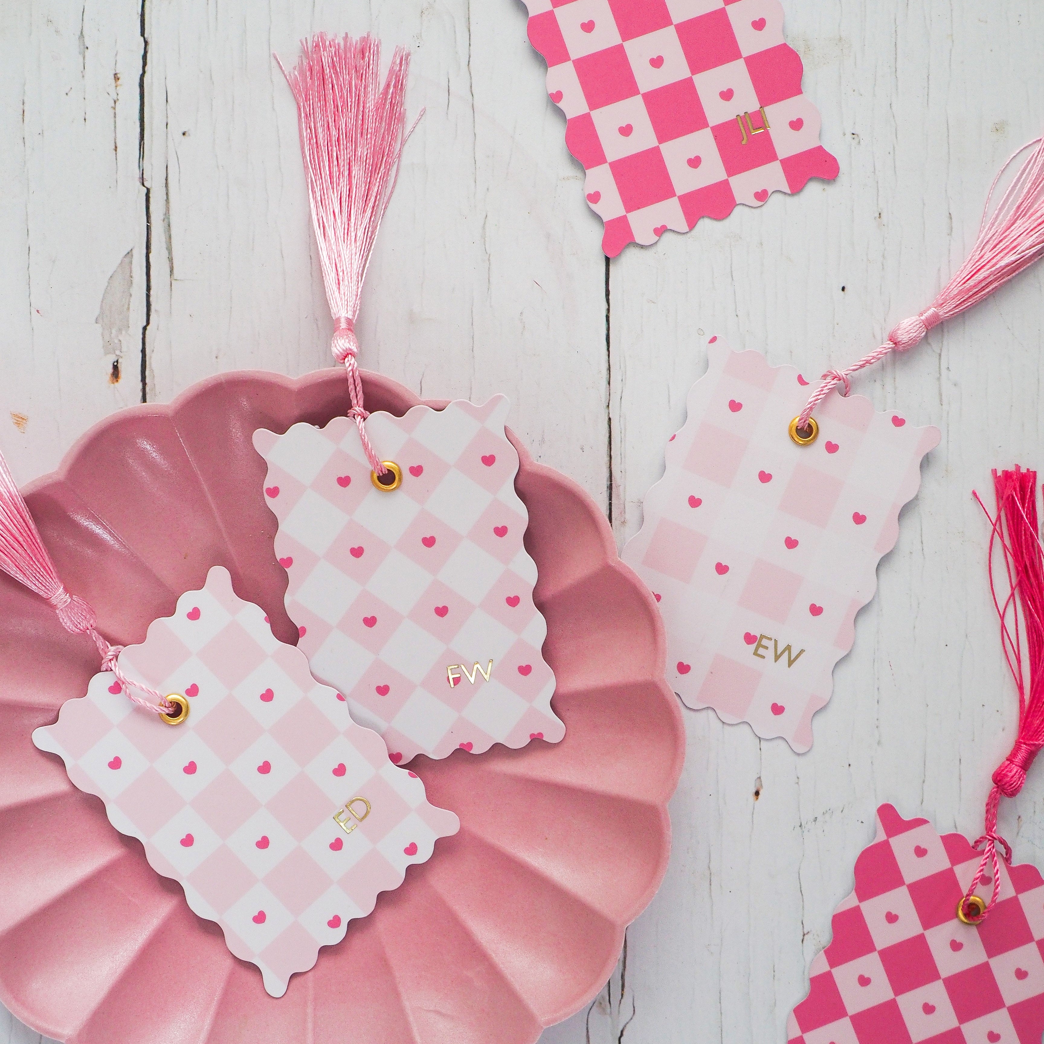 Decorative pink and white checkered tags with tassels on a wooden surface