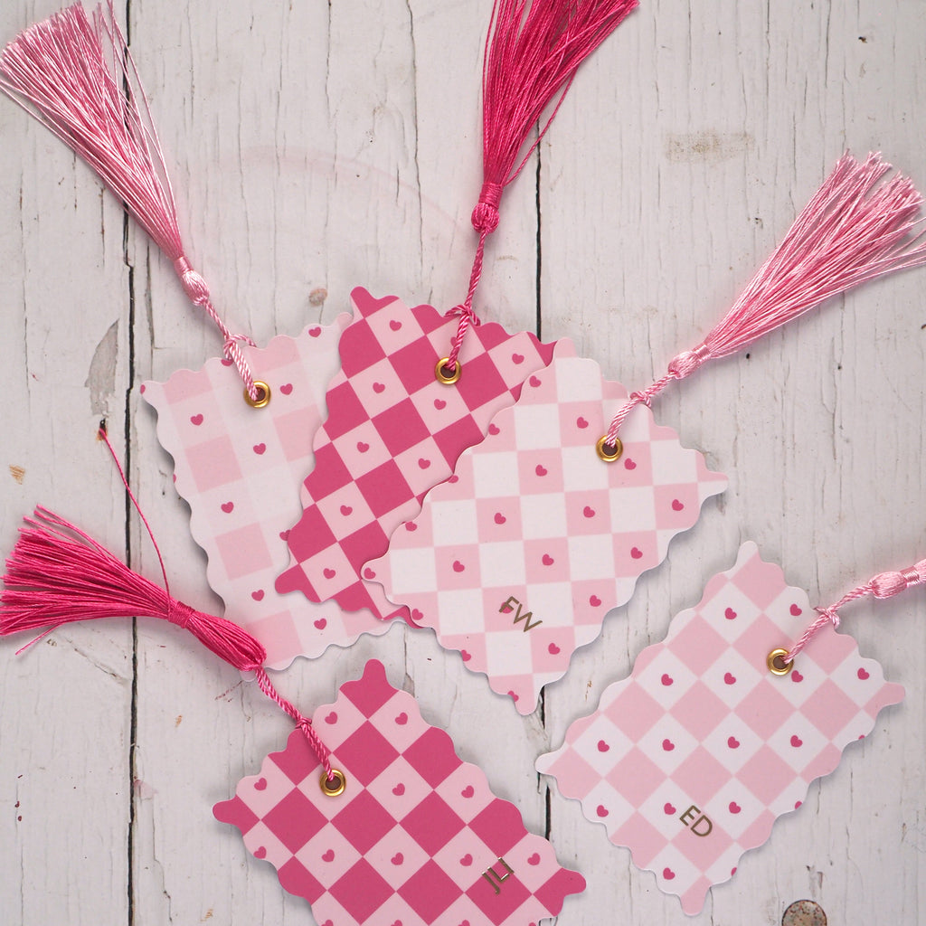 Pink and white chequered bookmark with tassels on a wooden surface
