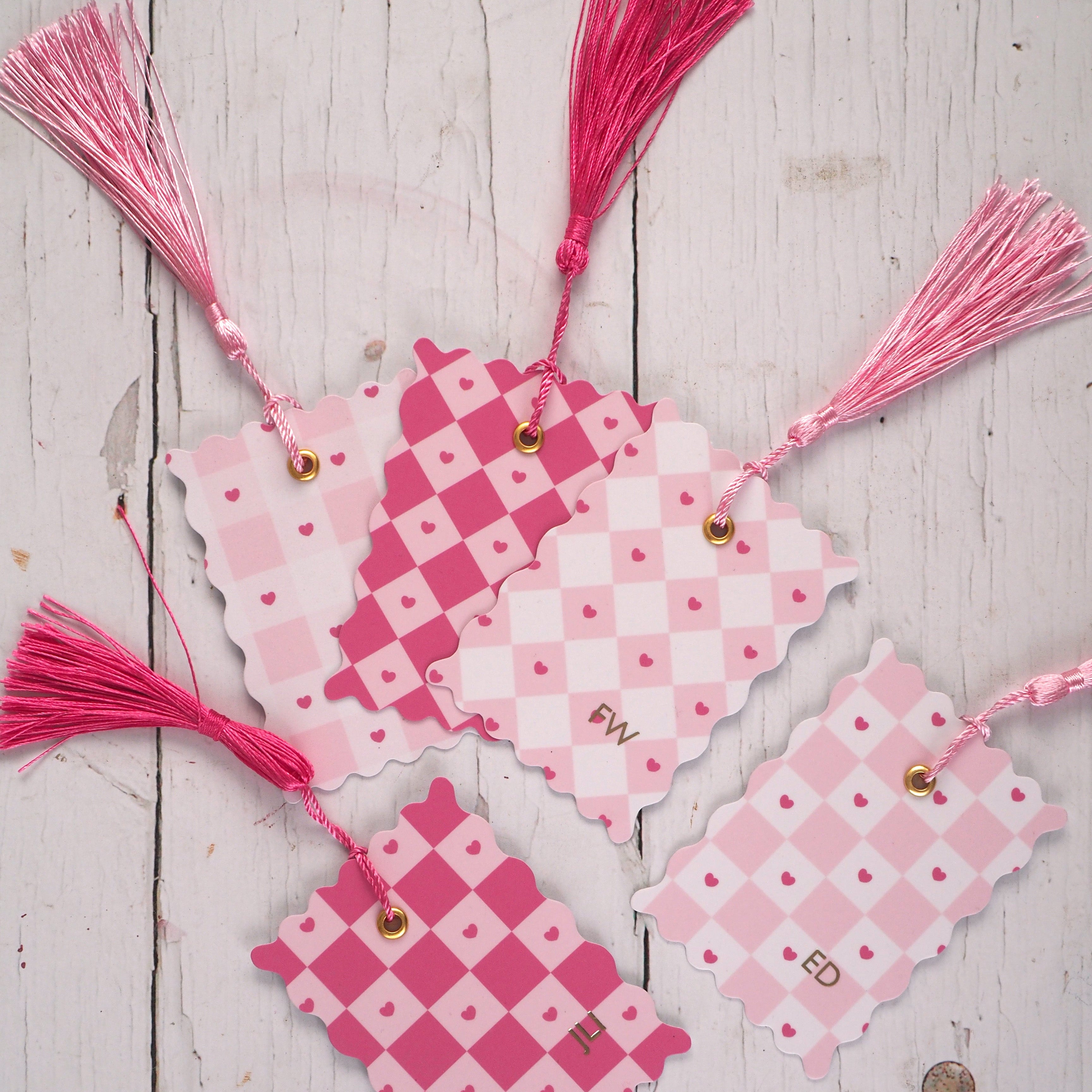 Pink and white chequered bookmark with tassels on a wooden surface