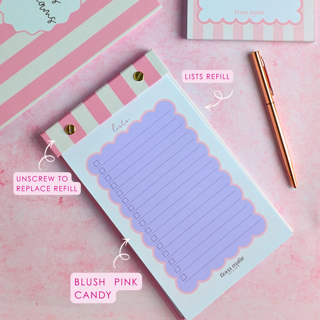 A styled flat-lay of pastel stationery on a pink surface, including a striped notepad, a refill packet labeled 'Lists Refill,' a pen, and a checklist notepad with a blush pink candy-themed label. Text callouts describe the items.