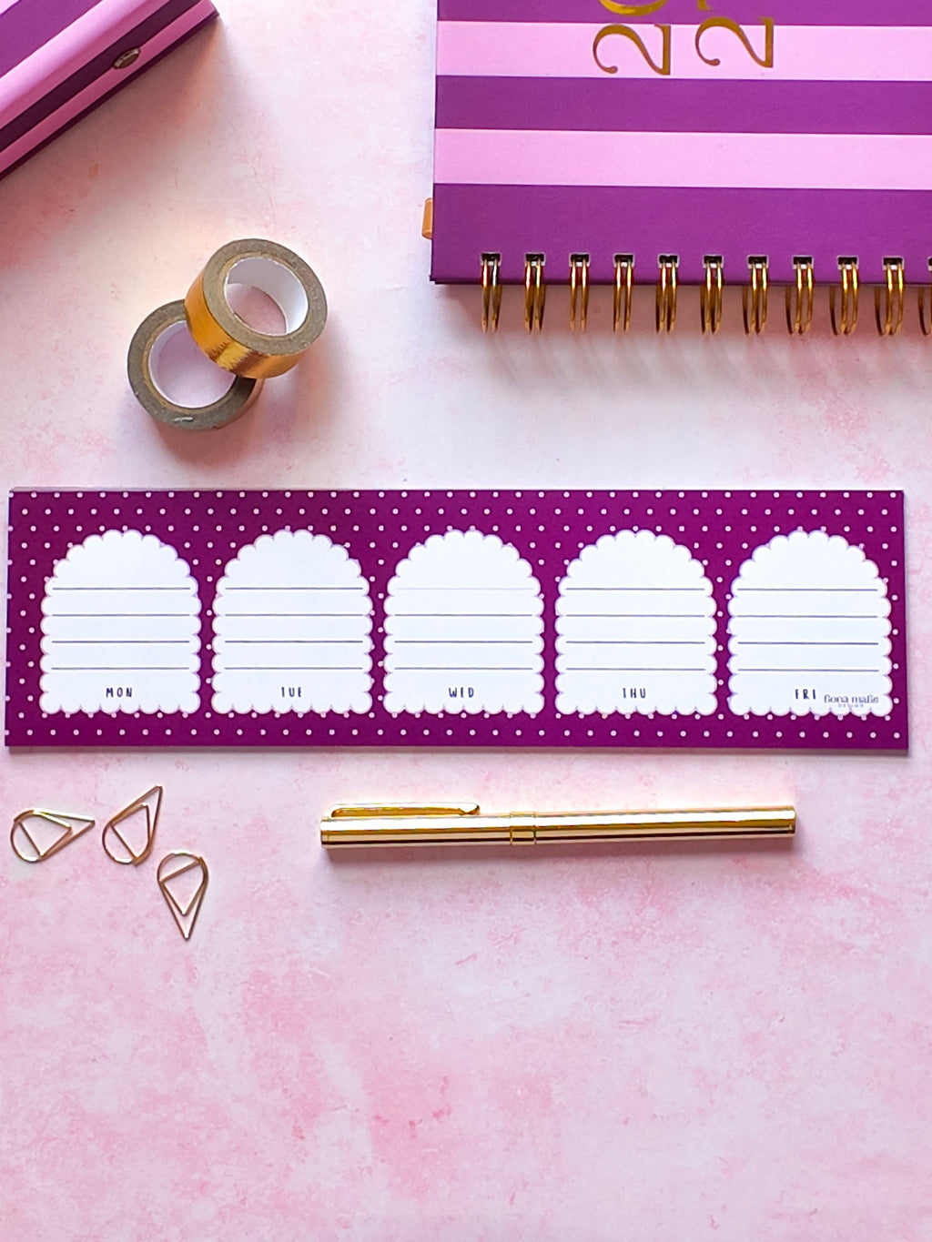 A purple and white arch-shaped planner insert sheet displayed on a pink background with coordinating stationery items including a purple spiral notebook, gold pen, washi tape, and paper clips.