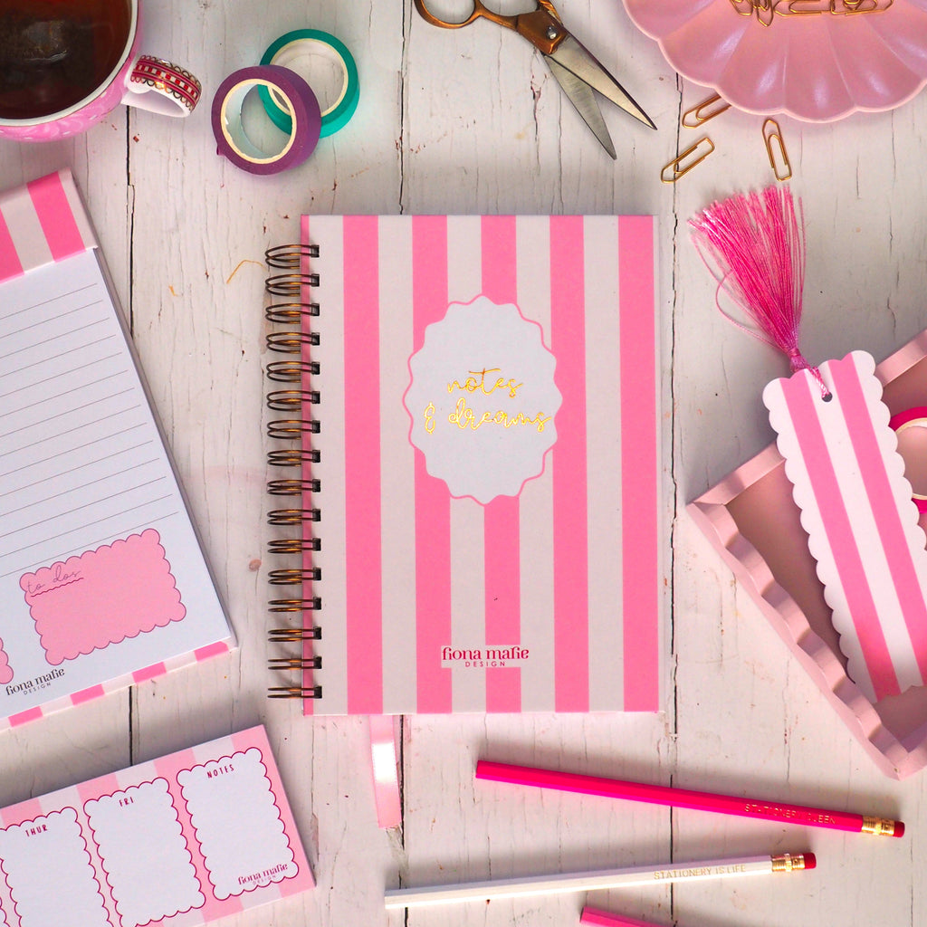 Pink stationery items including notebooks, stickers, and a cup of tea on a wooden surface.