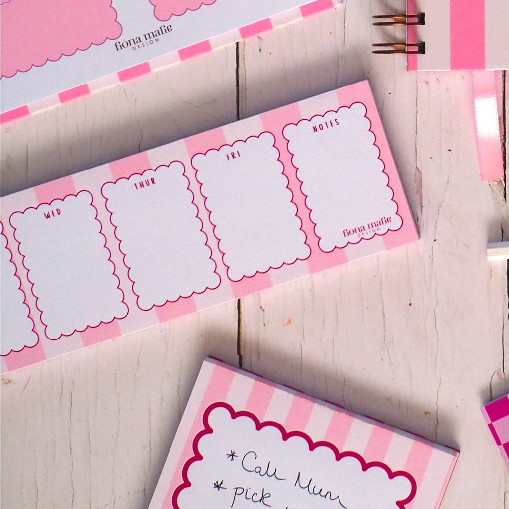 Pink stationery items including notebooks, stickers, and a cup of tea on a wooden surface.