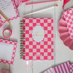 Pink checkered notebook with stationery items on a wooden surface