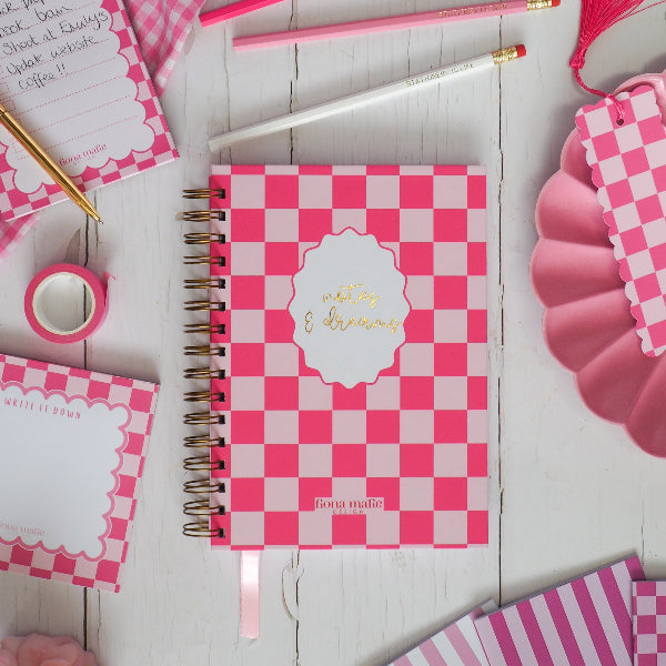 Pink checkered notebook with stationery items on a wooden surface