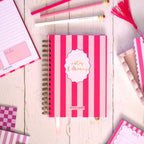 Pink and white striped stationery items on a wooden surface with a cup of tea.