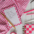Pink checkered notepad with stationery items on a wooden surface