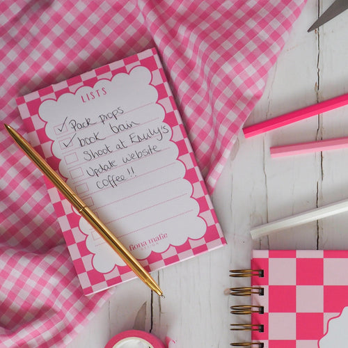 Pink checkered notepad with stationery items on a wooden surface