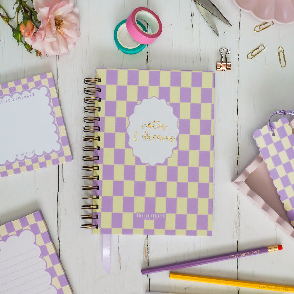 Lilac and pastel yellow scalloped checkered notebooks with stationery items on a wooden surface