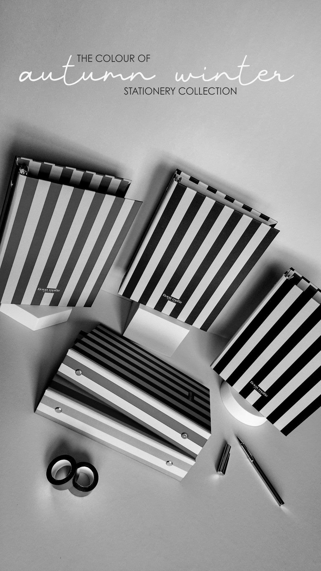 A styled flat-lay of autumn-themed stationery featuring black and white striped notebooks, a matching striped folder, a pen, and washi tape on a light gray background, with the text 'THE COLOUR OF autumn winter STATIONERY COLLECTION' at the top.