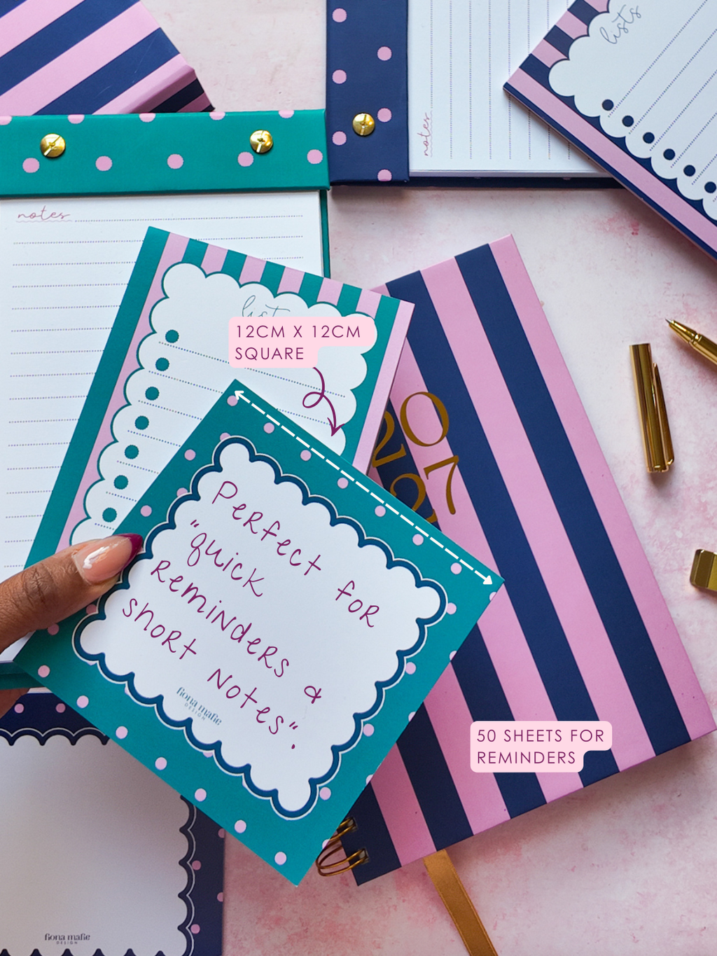 A hand holds a teal and pink polka-dot memo with handwritten text, surrounded by matching pink, navy, and teal striped and polka-dot stationery items on a light pink background.