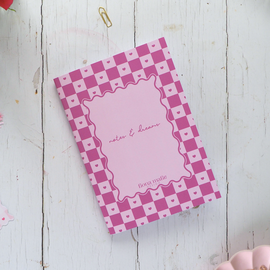 Pink checkered notebook with decorative items on a white wooden surface