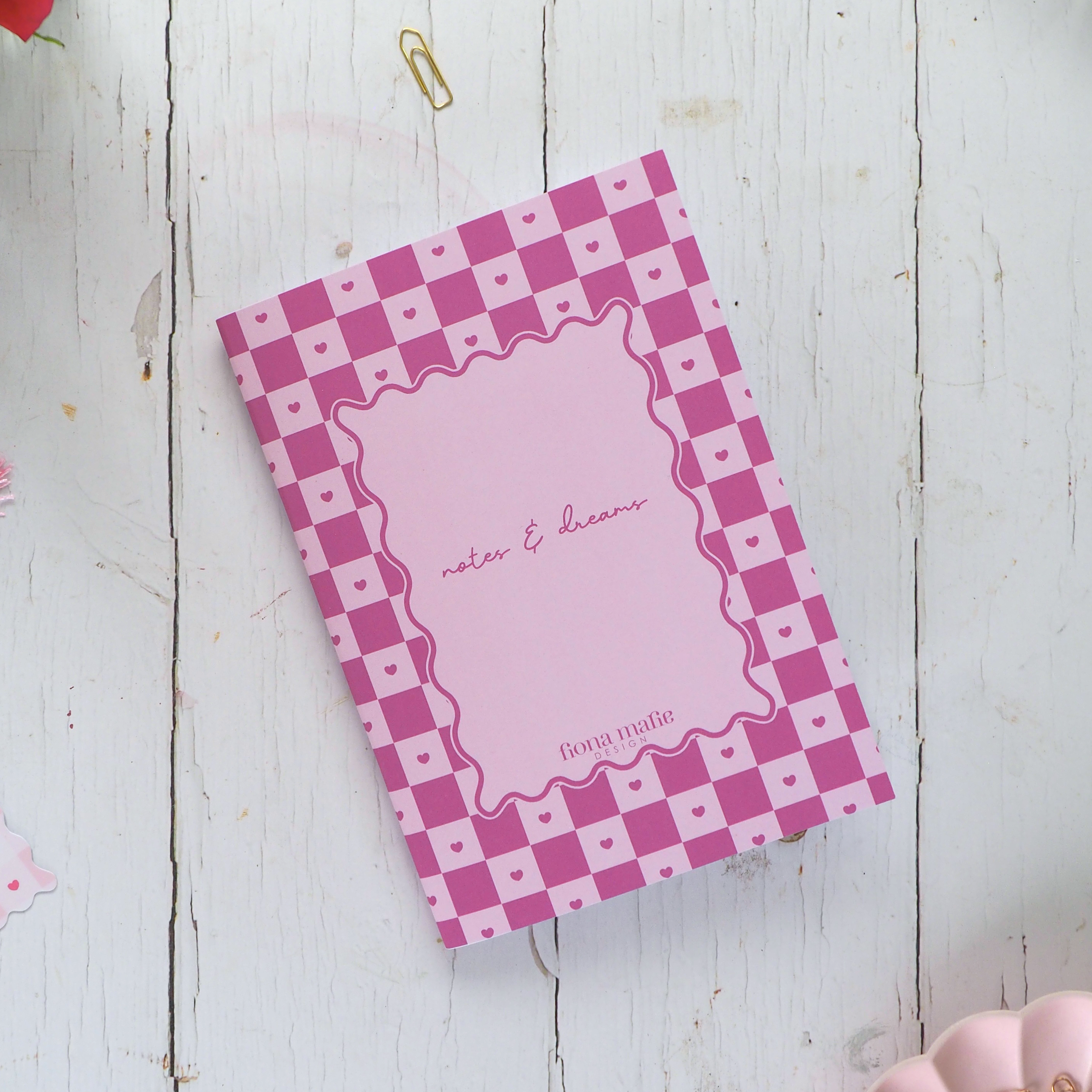 Pink checkered notebook with decorative items on a white wooden surface