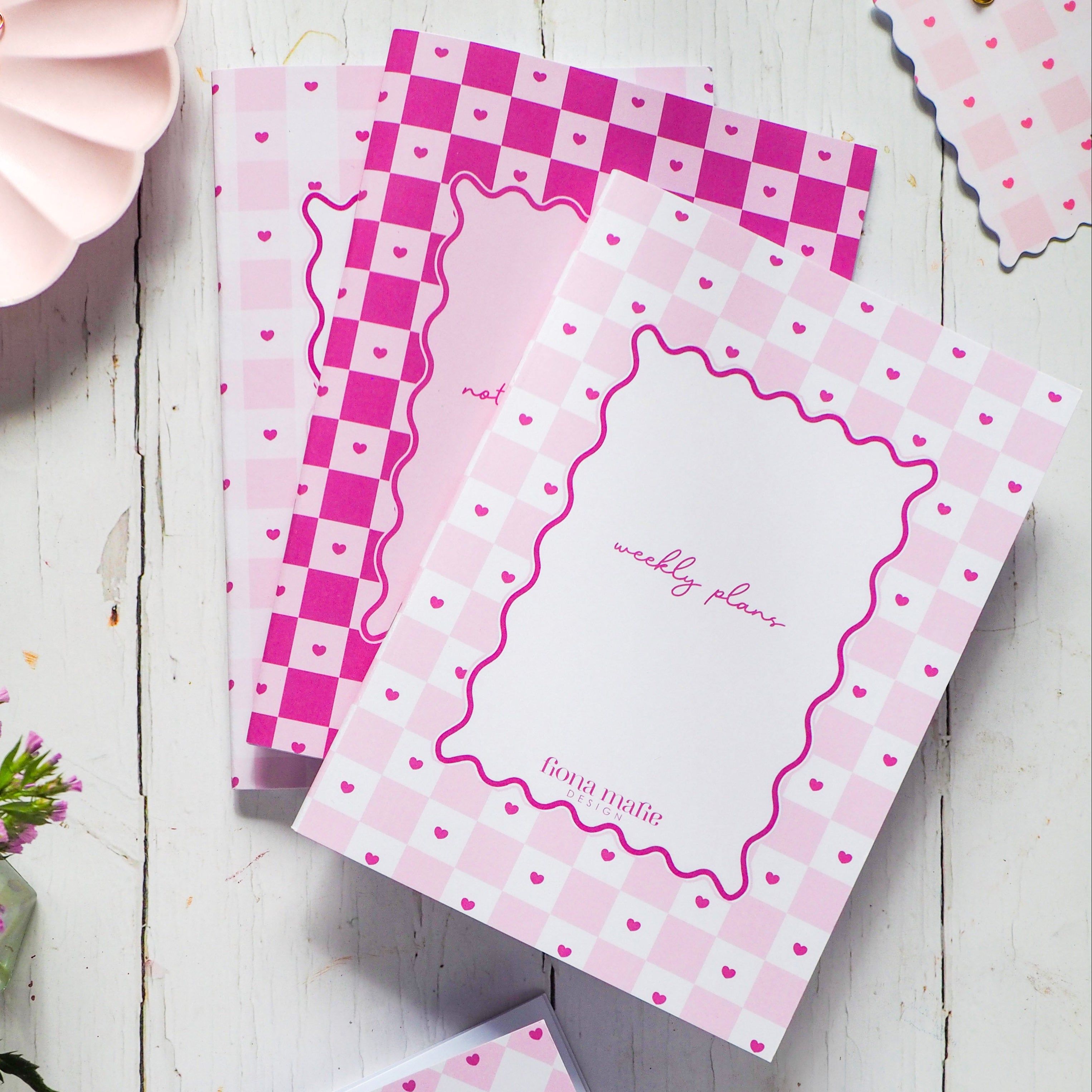 Pink stationery items with checkered and floral designs on a wooden surface.