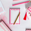 Pink and white striped notepad with a gold pen on a light pink background