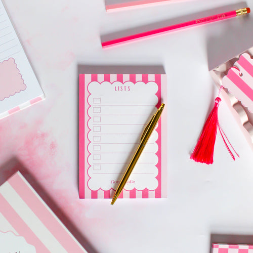 Pink and white striped notepad with a gold pen on a light pink background