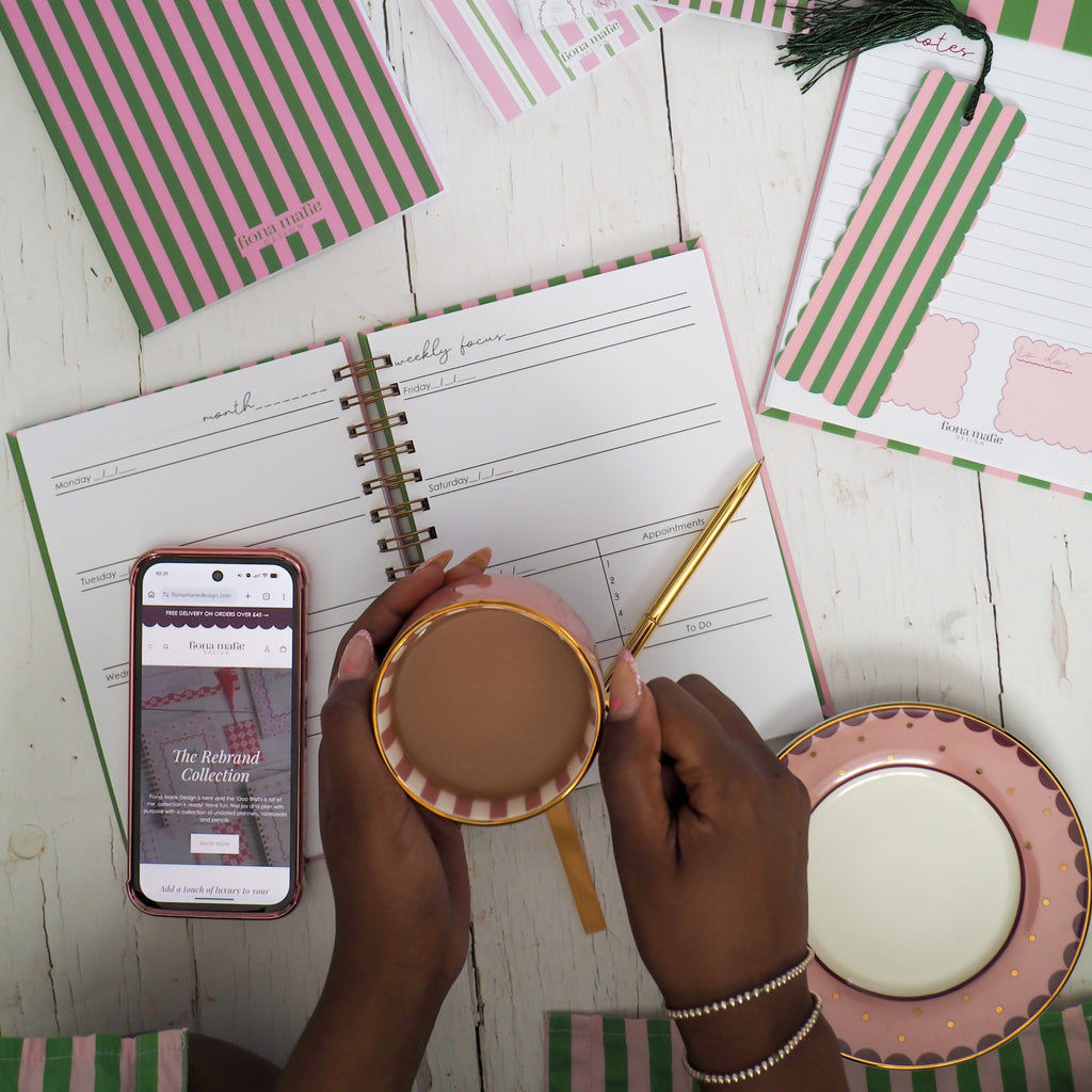 Person holding a cup of coffee with a planner and stationery items on a wooden surface