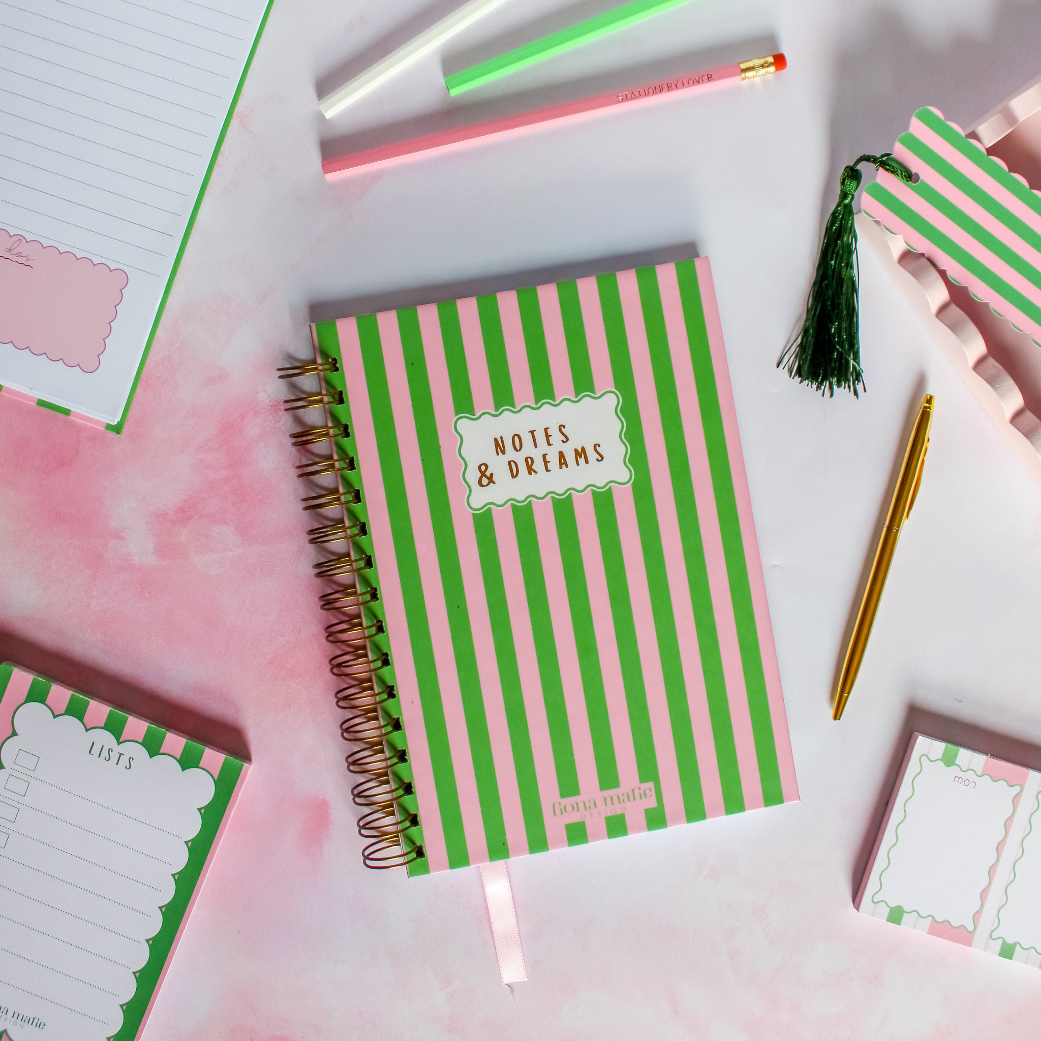 Notebook with green and pink striped cover on a white surface with stationery items.
